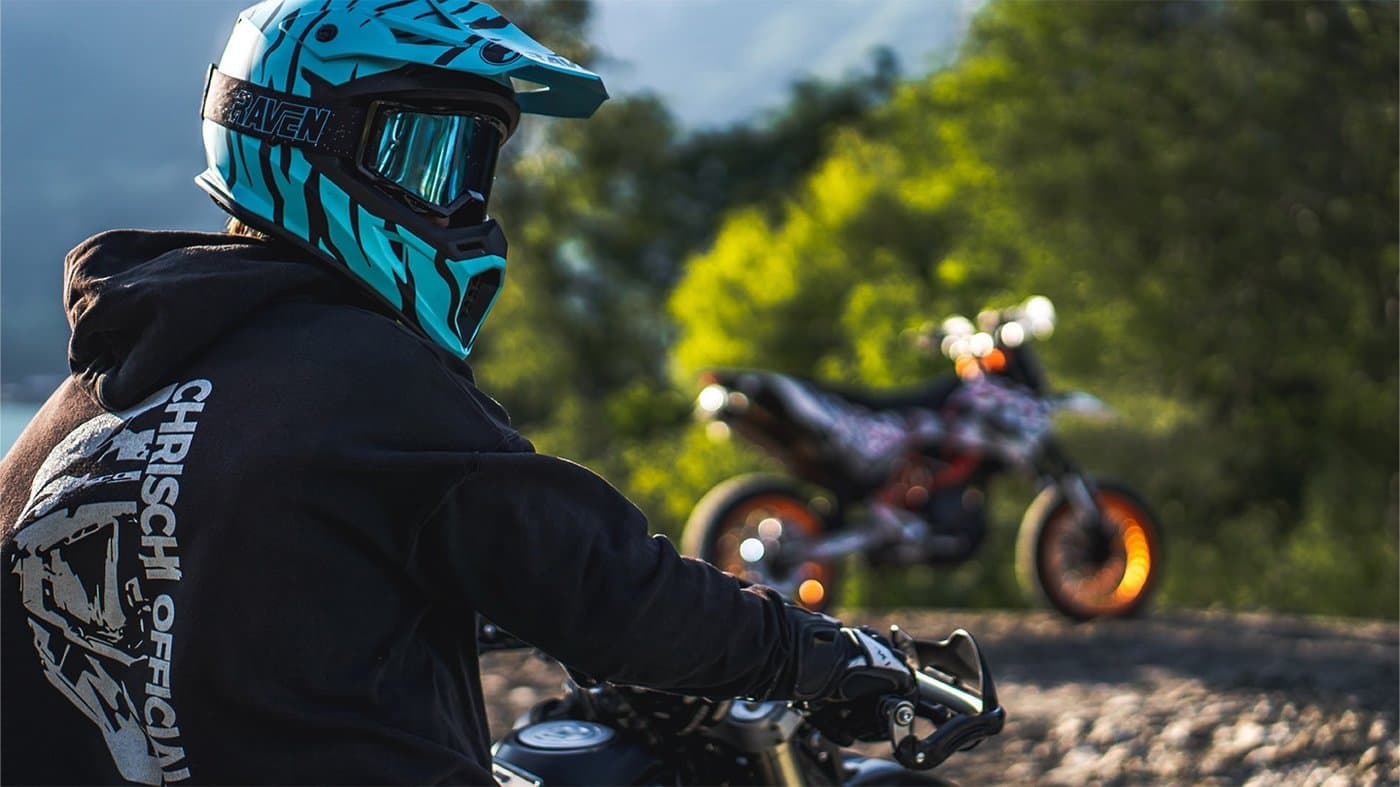 Motorradfahrer mit blauem Helm vor einem zweiten Motorrad
