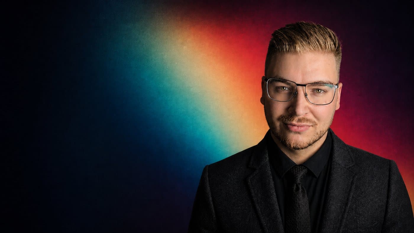 Portrait von Christoph Herrmann im dunklen Anzug vor farbigem Hintergrund